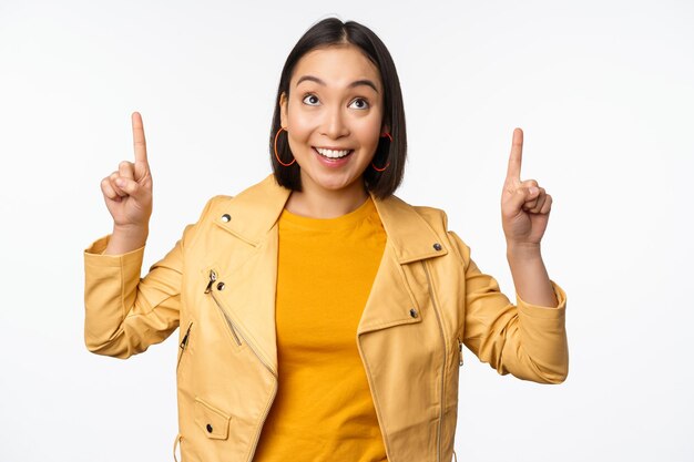 Imagen de una mujer morena asiática sonriente señalando con el dedo hacia arriba mostrando un anuncio con cara feliz posando sobre fondo blanco