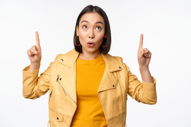 Imagen de una mujer morena asiática sonriente señalando con el dedo hacia arriba mostrando un anuncio con cara feliz posando sobre fondo blanco