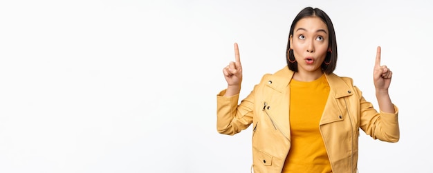 Imagen de una mujer morena asiática sonriente señalando con el dedo hacia arriba mostrando un anuncio con cara feliz posando sobre fondo blanco