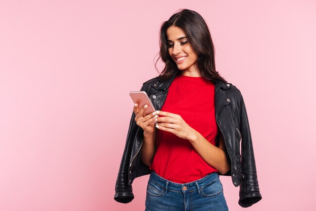 Imagen de mujer morena sonriente con smartphone sobre rosa