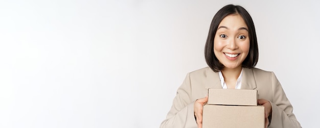 Imagen de una mujer de negocios vendedora asiática dando cajas con el pedido entregado al cliente de pie en traje sobre fondo blanco.