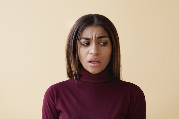 Foto gratuita imagen de mujer de raza mixta joven atractiva frustrada infeliz en ropa elegante con expresión facial perpleja preocupada, mirando hacia abajo y abriendo la boca, diciendo algo indeciso.