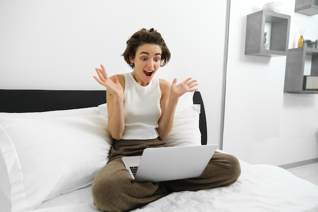 Foto gratuita la imagen de una mujer sentada en la cama mirando su teléfono inteligente con una expresión de cara sorprendida y conmocionada ha