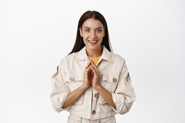 Imagen de una mujer sonriente esperanzada con los dedos y mirando la cámara, saboreando algo interesante, esperando ganancias, teniendo algo intrigante en mente, fondo blanco. copia espacio