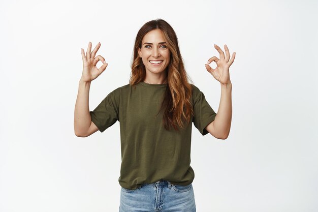 Imagen de una mujer sonriente de mediana edad con una piel perfecta, una sonrisa blanca, que muestra el signo de OK OK, aprueba y elogia la increíble tienda, recomienda el servicio de la empresa, fondo blanco