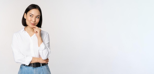 La imagen de una mujer sonriente pensativa tiene una idea planeando intrigar mirando a un lado y pensando de pie en una blusa blanca de oficina contra el fondo del estudio