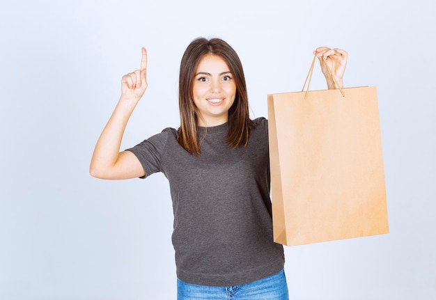 Imagen de mujer sonriente sosteniendo una bolsa de papel y apuntando hacia arriba con el dedo índice.