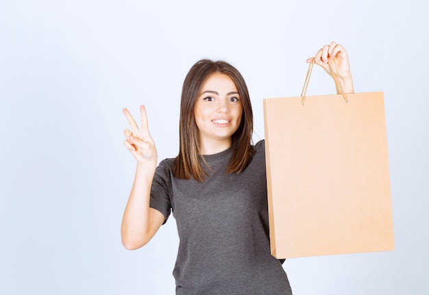 Imagen de mujer sonriente sosteniendo una bolsa de papel y mostrando el signo de la victoria.