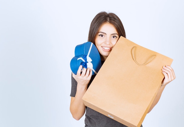 Imagen de mujer sonriente sosteniendo un regalo en forma de corazón y una bolsa de papel en las manos.