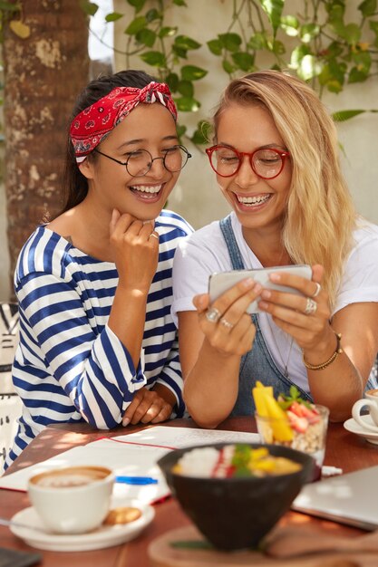 Imagen de mujeres multiétnicas alegres de aspecto agradable ver comedia en el teléfono celular