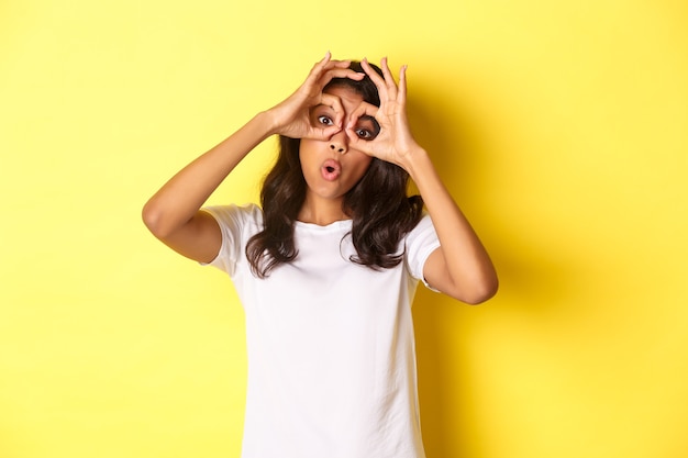 Imagen de niña afroamericana feliz y divertida haciendo gafas de dedo y mirando a través de ellos