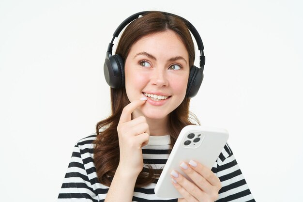 Foto gratuita imagen de una niña con auriculares sonriendo mientras piensa tomando decisiones sosteniendo un teléfono inteligente tomando decisiones