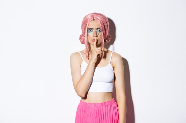 Imagen de una niña enojada con el ceño fruncido con peluca rosa y maquillaje de halloween, callando a alguien, regañando a la persona por ser demasiado ruidosa, de pie.