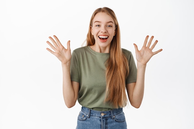 Imagen de una niña feliz emocionada y sorprendida, un apretón de manos saltando de alegría y riendo alegre, de pie en camiseta contra el fondo blanco.