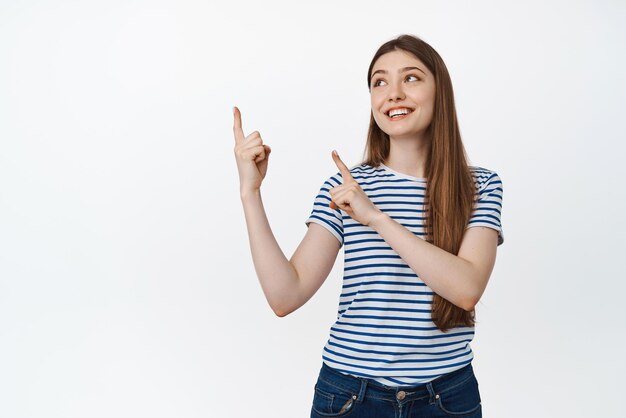 Imagen de una niña feliz sonriente señalando y mirando el espacio vacío de la esquina superior izquierda para el logotipo de venta de pie sobre fondo blanco