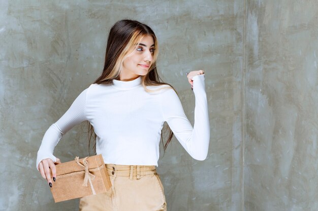 Imagen de una niña modelo sosteniendo un papel presente sobre piedra