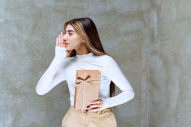 Imagen de una niña modelo sosteniendo un papel presente sobre piedra