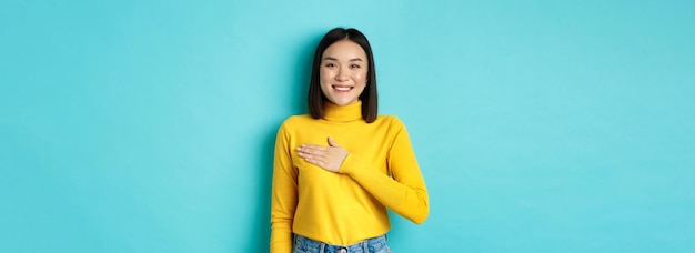 Foto gratuita imagen de una orgullosa mujer asiática sonriente sosteniendo la mano en el corazón mostrando respeto al himno nacional de pie