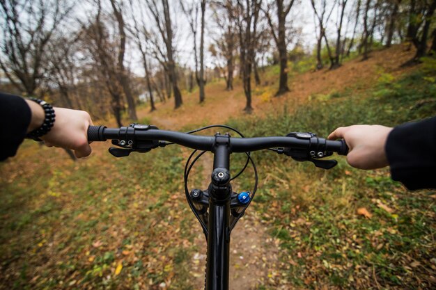 Imagen de primer plano del ciclista hombre manos en el manillar montando bicicleta de montaña en el sendero en el parque de otoño