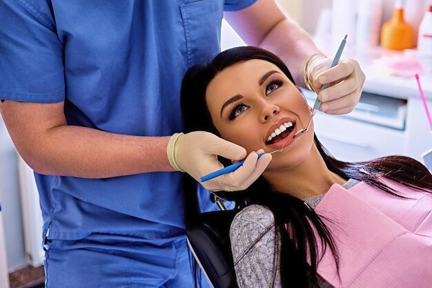 Imagen de primer plano de un dentista que examina los dientes de una mujer en odontología.