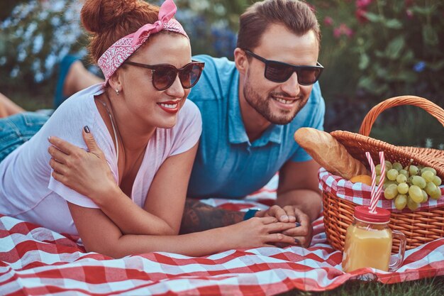 Imagen de primer plano de una feliz pareja de mediana edad durante una cita romántica al aire libre, disfrutando de un picnic mientras se acuesta en una manta en el parque.