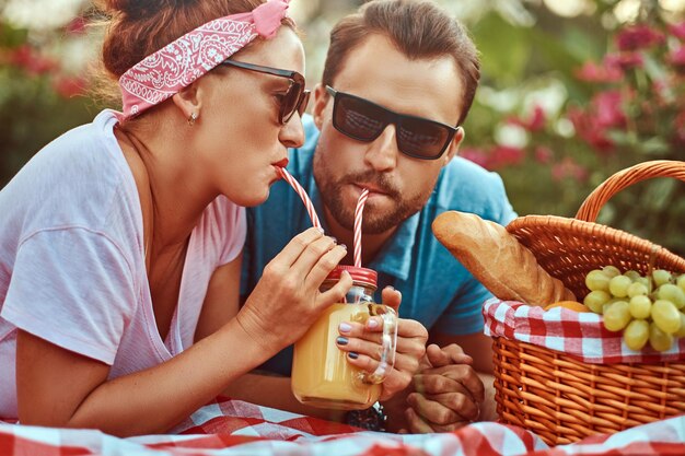 Imagen de primer plano de una feliz pareja de mediana edad durante una cita romántica al aire libre, disfrutando de un picnic mientras se acuesta en una manta en el parque.