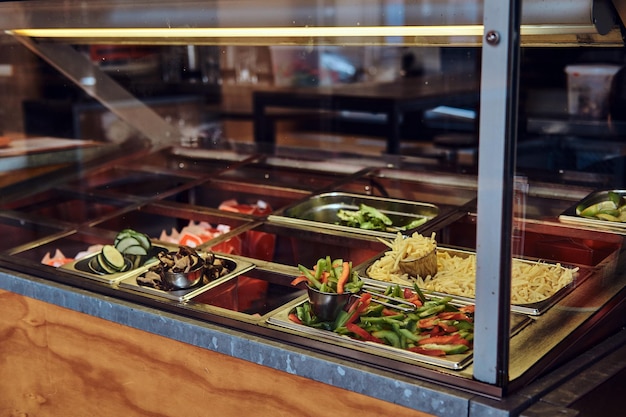 Imagen de primer plano de recipientes metálicos con diferentes verduras para llevar comida rápida en la cafetería.