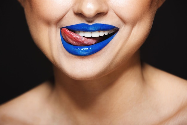 Imagen de primer plano de la sonrisa de una chica alegre con lápiz labial azul Lengua lamiendo labios