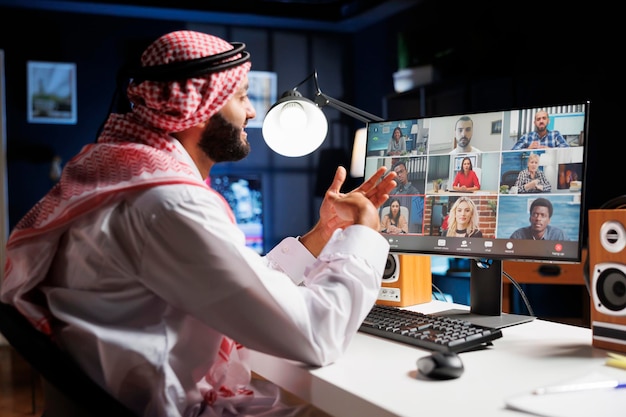 Imagen que muestra a un hombre de Oriente Medio vestido con ropa tradicional hablando con un grupo de personas en la pantalla de su computadora Un hombre islámico conversando con su equipo en una conferencia telefónica