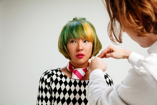 Imagen que muestra a una mujer adulta en la peluquería. Disparo de estudio de elegante joven con elegante corte de pelo corto y cabello colorido sobre fondo gris y manos de peluquero.