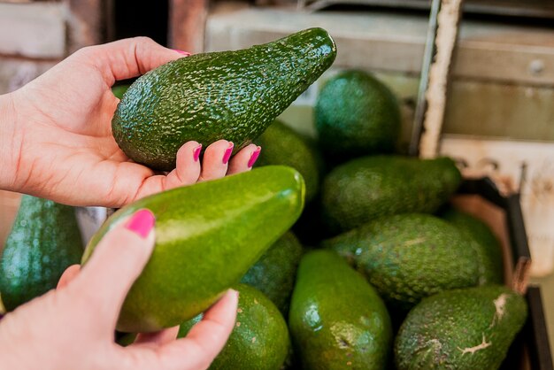 Imagen recortada de un cliente que elija los aguacates en el supermercado. Cerca de la mano de la mujer la celebración de aguacate en el mercado. Venta, compras, comida, consumismo y concepto de la gente