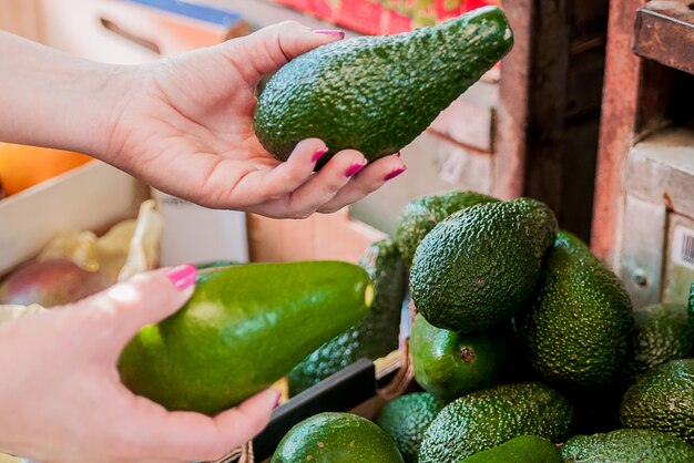 Imagen recortada de un cliente que elija los aguacates en el supermercado. Cerca de la mano de la mujer la celebración de aguacate en el mercado. Venta, compras, comida, consumismo y concepto de la gente