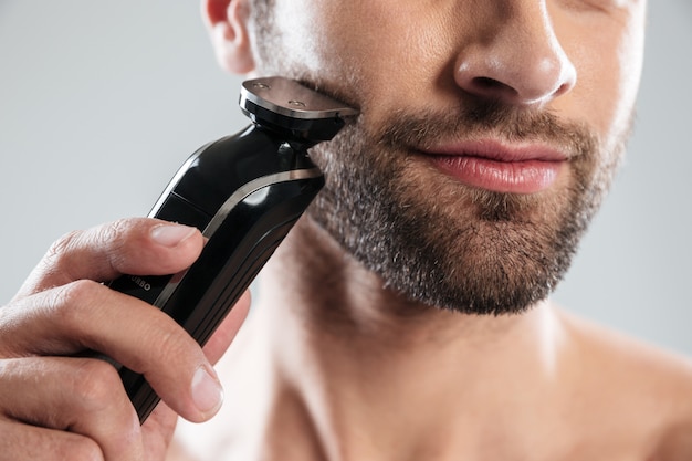 Foto gratuita imagen recortada de un hombre barbudo con maquinilla de afeitar eléctrica
