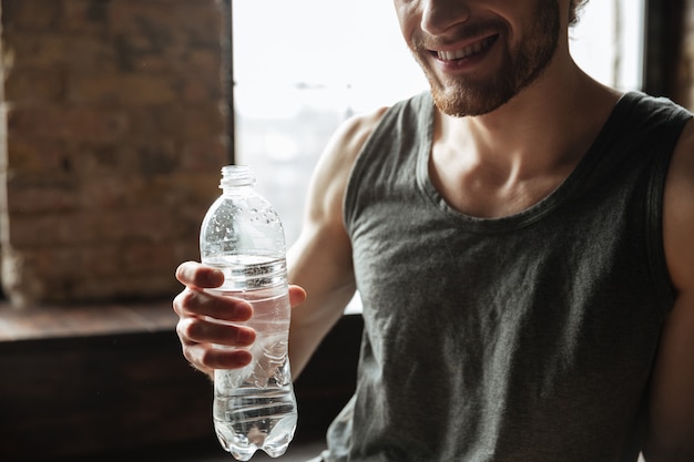 Imagen recortada de un hombre sonriente de fitness con botella de agua