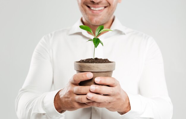 Imagen recortada del hombre sonriente joven que sostiene la planta.