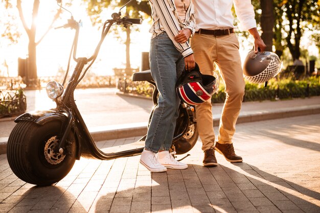 Imagen recortada de la joven pareja africana posando cerca de la moto moderna en el parque