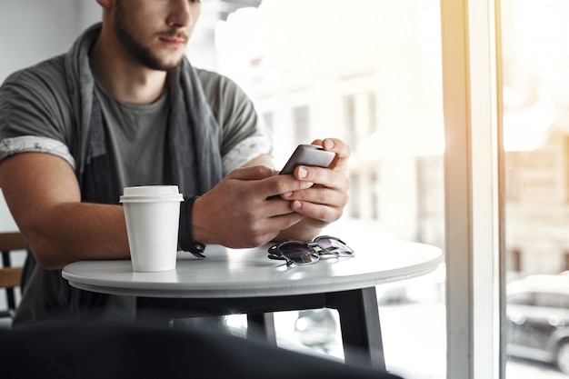 Imagen recortada del mensaje de texto del hombre en el teléfono en el café.