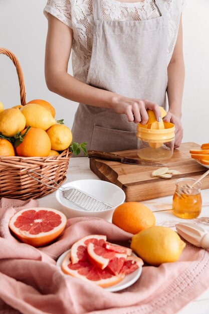 Imagen recortada de mujer exprime el jugo de una fruta cítrica.