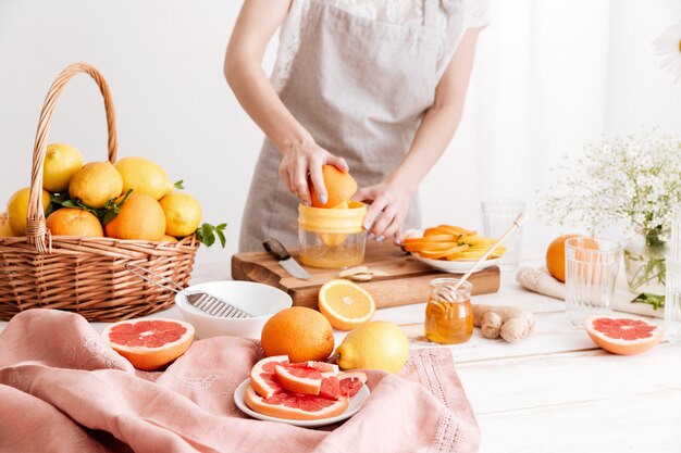 Imagen recortada de mujer exprime el jugo de una fruta cítrica.