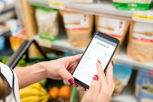 Imagen recortada de mujer revisando la lista de compras en el teléfono inteligente en la tienda de comestibles