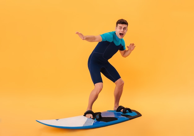 Imagen de surfista asustado en traje de neopreno usando tabla de surf como en olas y gritando