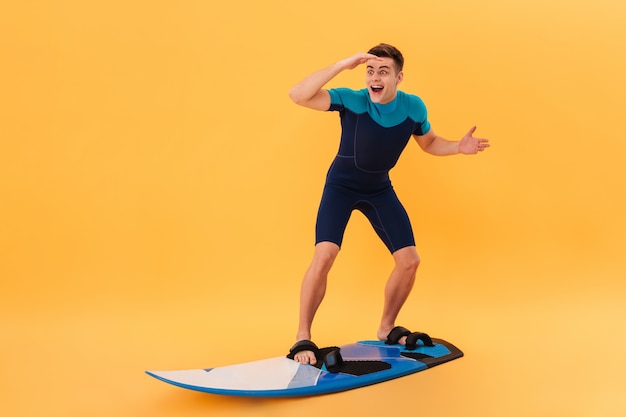 Imagen de surfista feliz sorprendido en traje de neopreno con tabla de surf como en la ola y mirando a otro lado