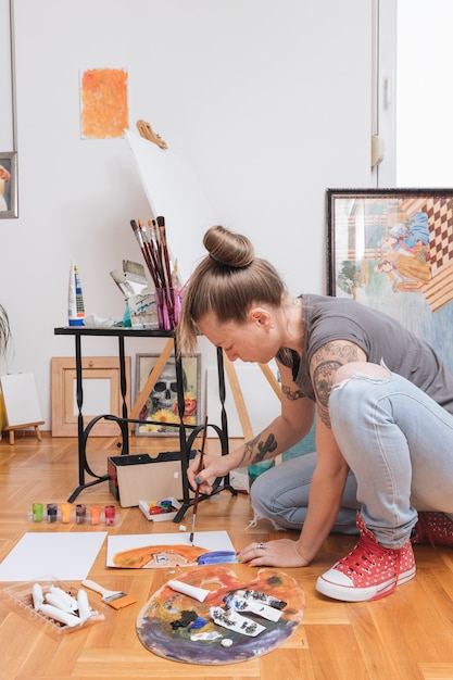 Foto gratuita imagen tatuada de la pintura del artista de sexo femenino joven que se sienta en piso