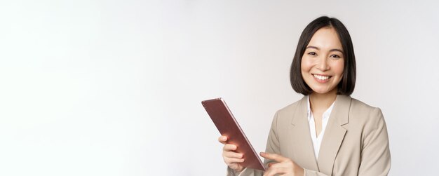 Imagen de una vendedora de negocios asiática sosteniendo una tableta digital y sonriendo trabajando con un puesto de gadgets