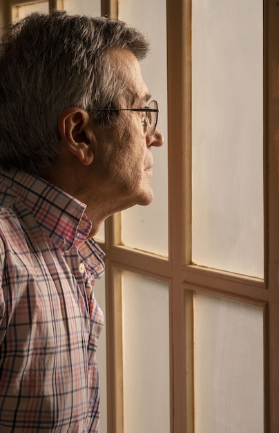 Foto gratuita imagen vertical de un anciano con gafas mirando por la ventana