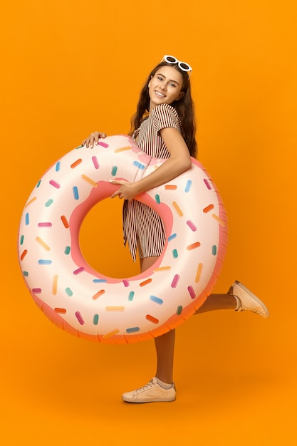 Imagen vertical de una chica guapa alegre que va a la playa con un círculo de goma.