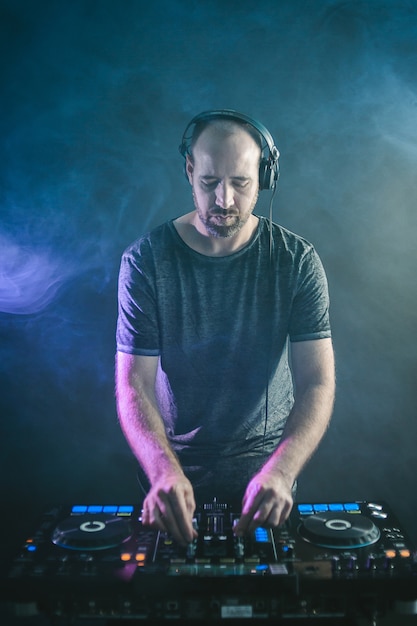Imagen vertical de un DJ masculino bajo las luces azules y el humo