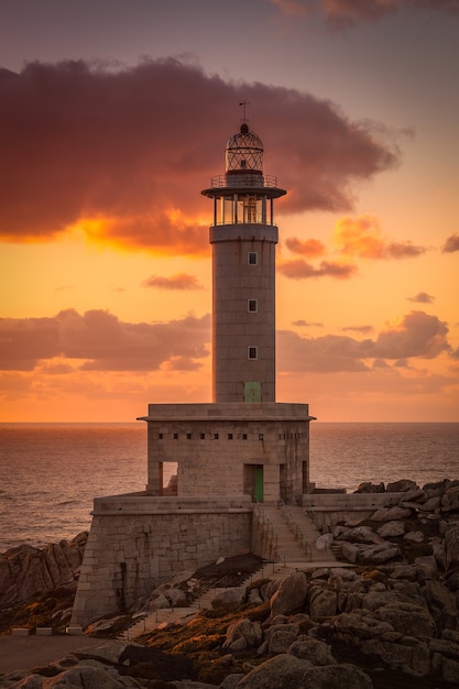 Imagen vertical del faro de Punta Nariga rodeado por el mar durante la puesta de sol en España