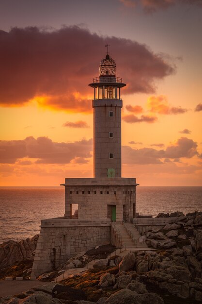 Imagen vertical del faro de Punta Nariga rodeado por el mar durante la puesta de sol en España