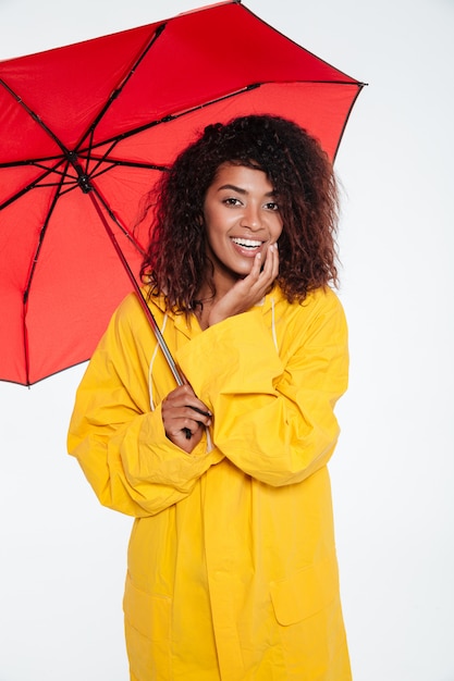 Imagen vertical de feliz mujer africana en impermeable posando